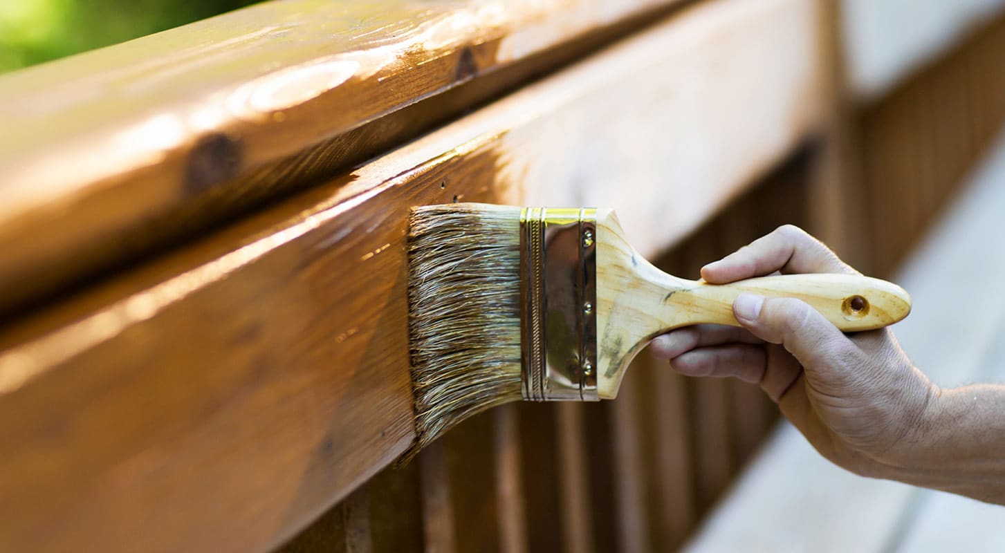 A person carefully painting a wooden railing with a brush, enhancing its appearance and protection.